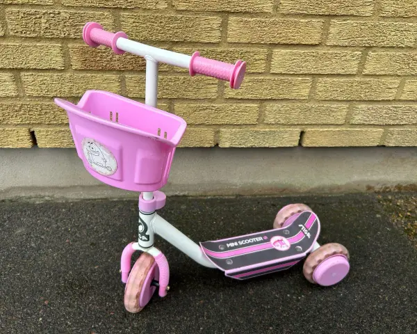 En rosa stiga sparkcykel trehjuling med korg framtill, redo för äventyr.