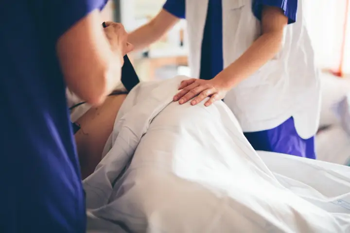 Två vårdgivare assisterar en gravid v 39. En av dem håller i en apparat, den andra lägger en hand på magen.