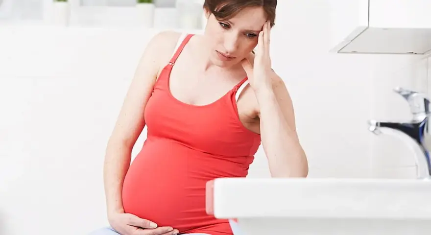 Gravid kvinna med handen mot pannan, känner sig illamående sent i graviditeten.