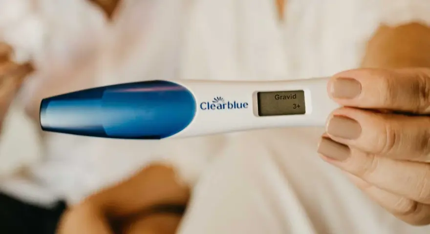 En hand håller en graviditetstest som visar "Gravid 3+". Tidiga tecken på graviditet kan vara spännande.