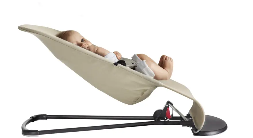 En bebis ligger bekvämt i en beige BabyBjörn babysitter.