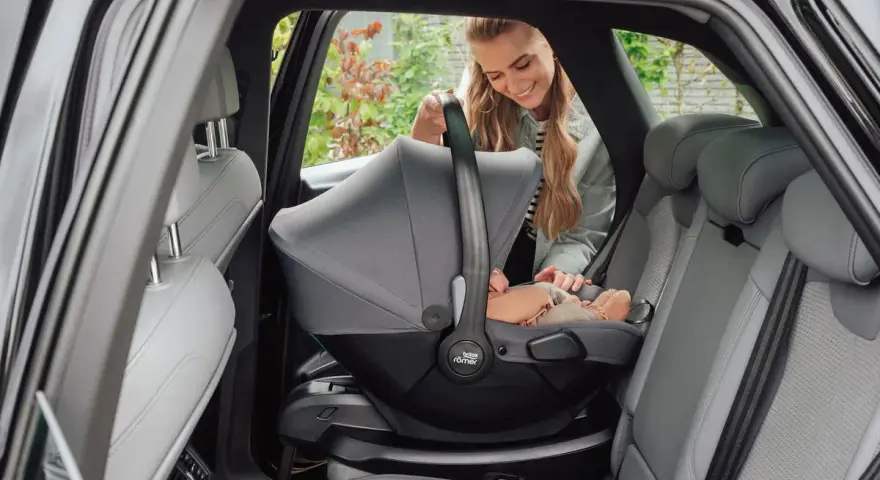 En leende mamma placerar en baby i en Britax Baby Safe Core bilbarnstol i en bil.