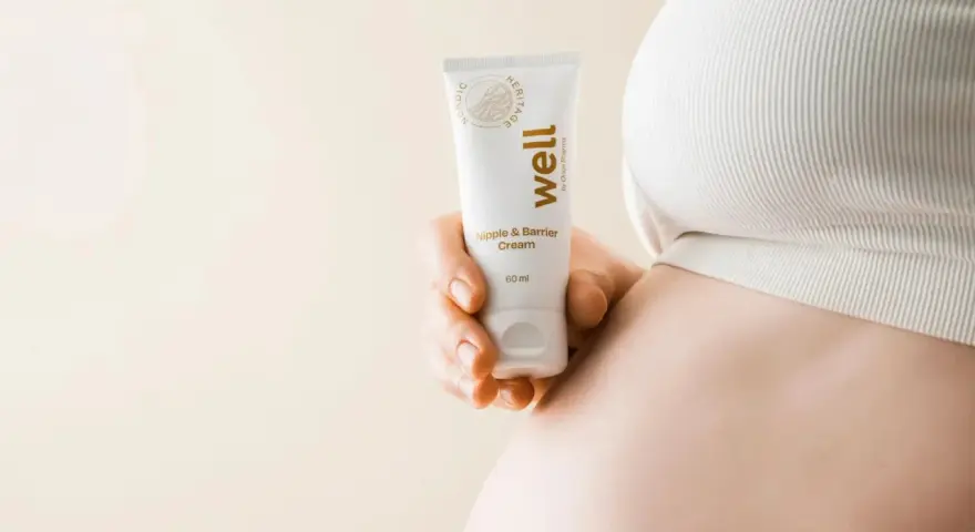 En hand håller en tub med "well Nipple & Barrier Cream", liknande Medela Purelan, nära en gravid mage.