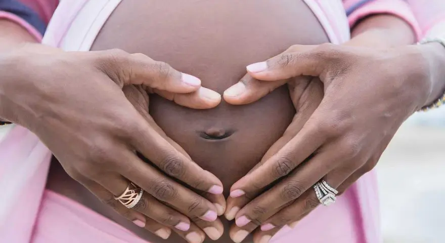 Gravid vecka 32, familjeliv. Händer formar ett hjärta runt magen.