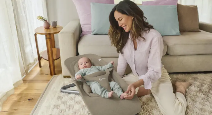 En leende mamma interagerar med sin bebis i en ergobaby babysitter.