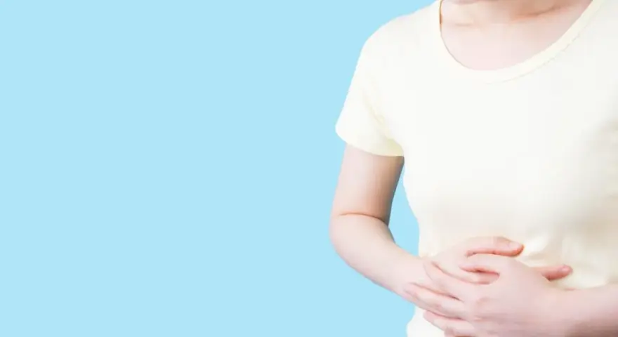 Kvinna håller sig om magen, upplever obehag som kan liknas vid IBS, graviditet eller magproblem.