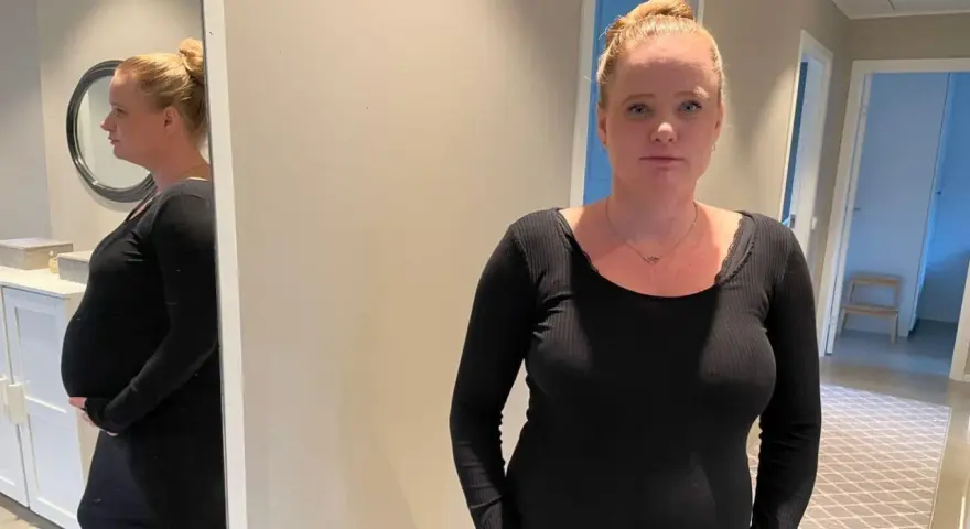 Gravid kvinna med stressad blick, med sin mage synlig. Hon funderar på hur hon ska hantera gravid stress på jobb.