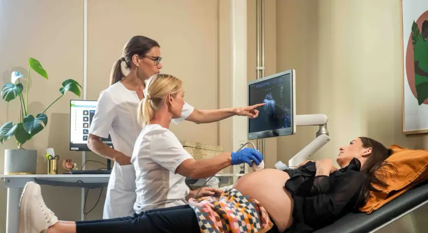 Två vårdgivare utför ett vaginalt ultraljud på en gravid kvinna. Bilden visar en skärm med ultraljudsbilder.