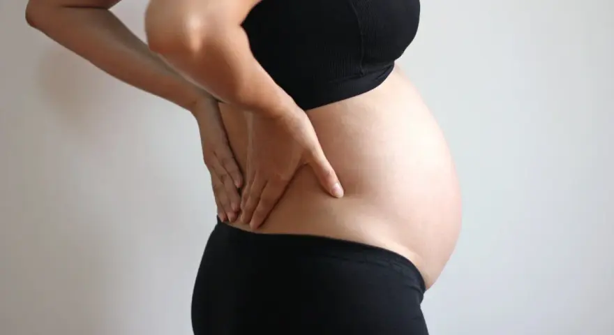 Gravid kvinna med händerna på ryggen, upplever ont i revbenen tidigt i graviditeten.