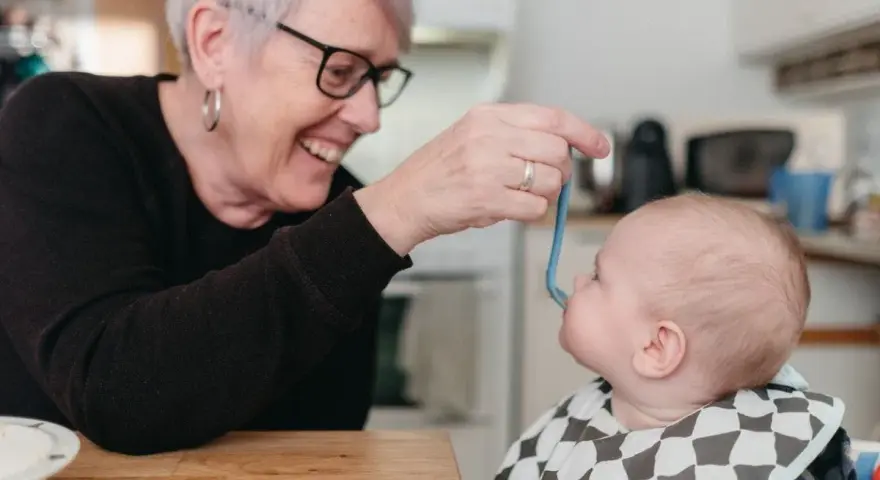 Glad mormor matar bebis med smakportioner. Första maten för en 4 månader gammal bebis.