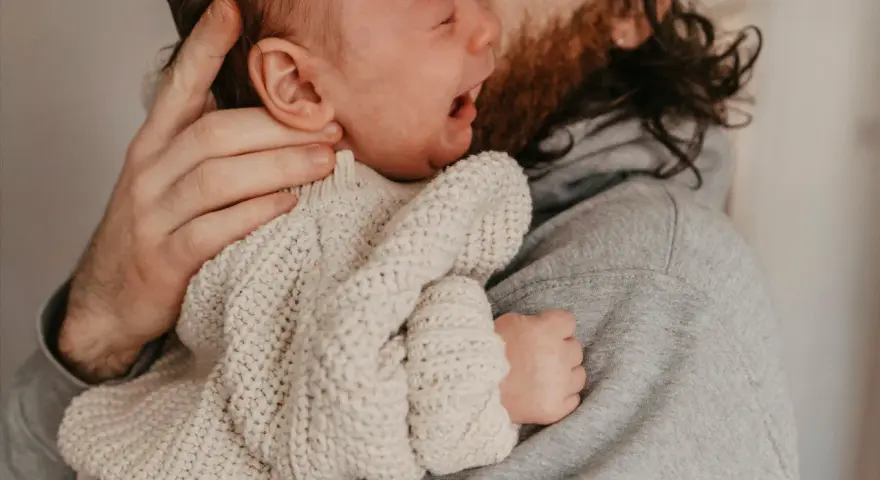 En bebis drar sig i håret medan den vilar i sin pappas famn.