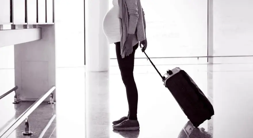 Gravid kvinna med resväska på flygplatsen, redo att flyga gravid.