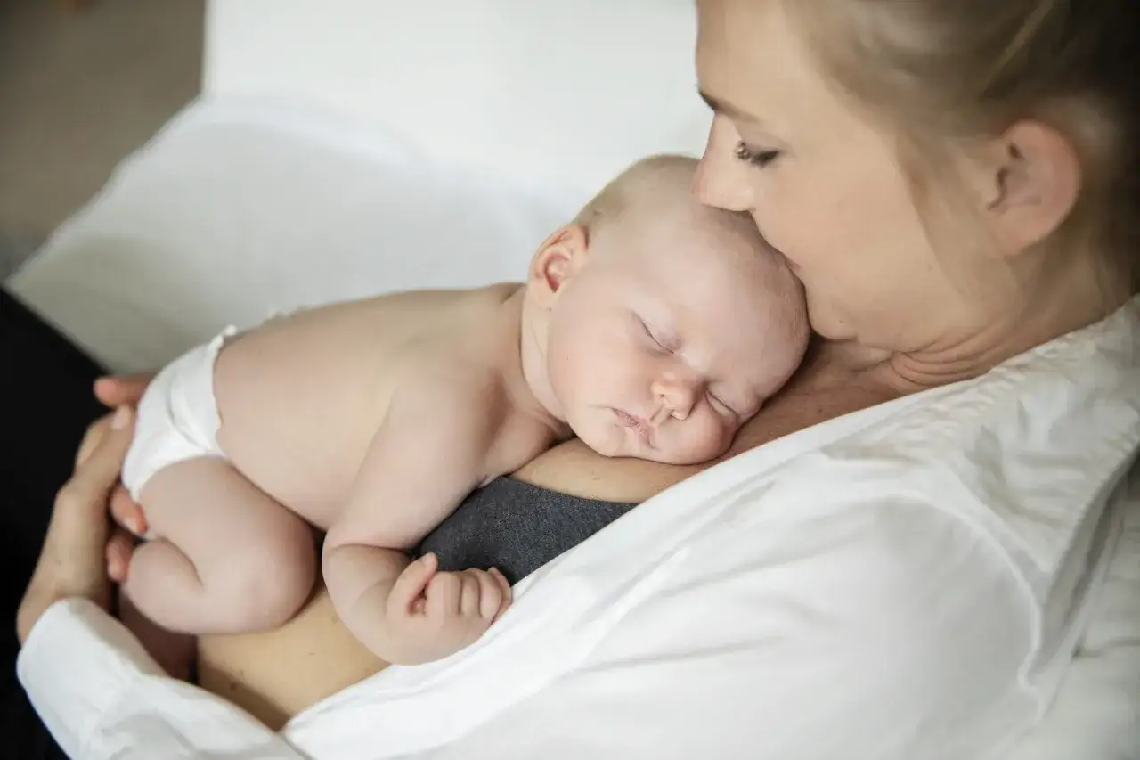 En mamma kysser sin sovande bebis som vilar mot hennes br&ouml;st. Ett &ouml;gonblick av lugn, som ett mjukt klickljud amning.
