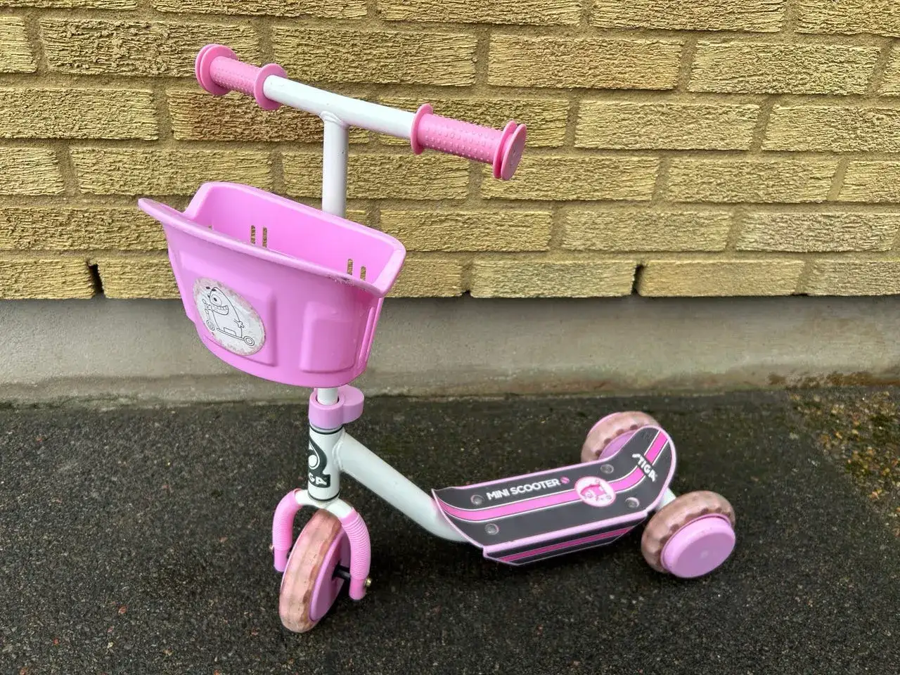 En rosa stiga sparkcykel trehjuling med korg framtill, redo f&ouml;r &auml;ventyr.