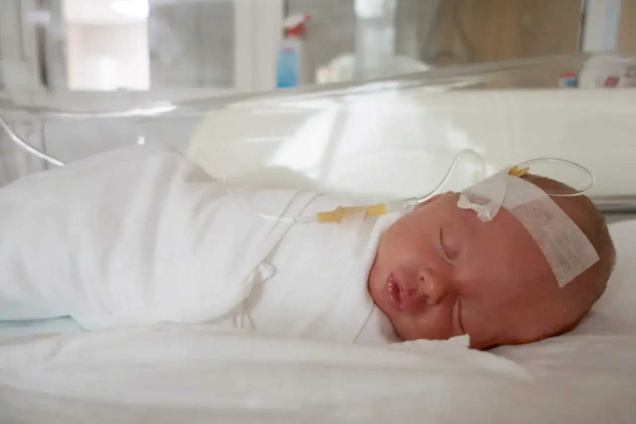 Nyf&ouml;dd bebis med dropp i huvudet, insvept i vitt. Liten mun &ouml;ppen, kanske lite irriterad hud runt munnen, som vid bebis diarre.