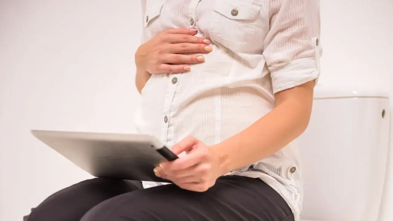 Gravid kvinna med brunt blod på toaletten, hon håller en surfplatta.