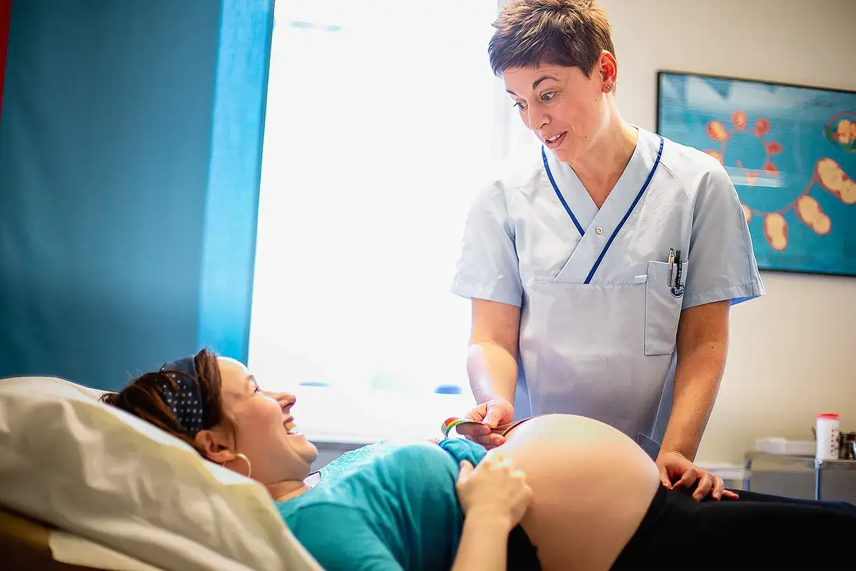 Barnmorska mäter magen på en glad, ibs gravid kvinna.