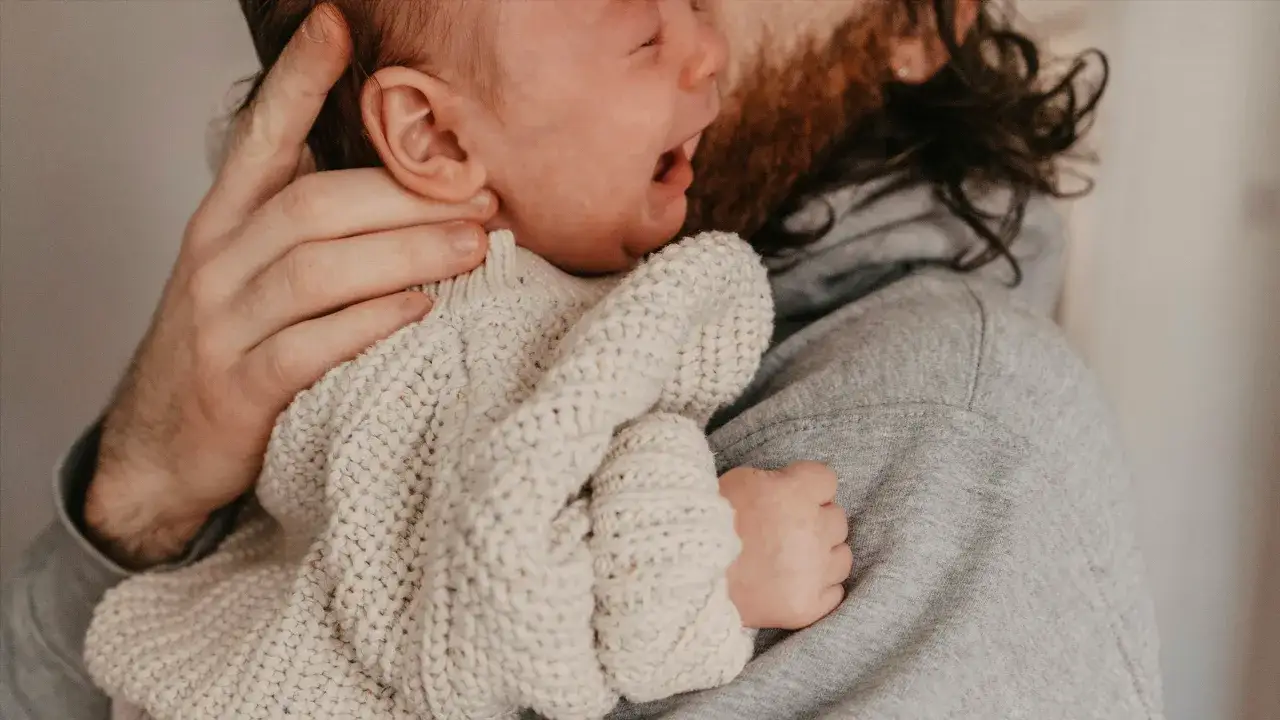 En bebis drar sig i håret medan den vilar mot sin pappas bröst.