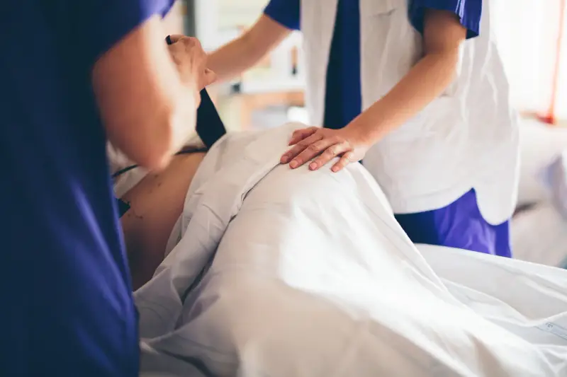 Två vårdgivare assisterar en gravid v 39. En av dem håller i en apparat, den andra lägger en hand på magen.