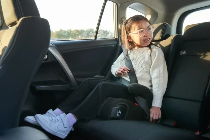 Flicka i bilens baksäte sitter på bälteskuddar och är fastspänd.